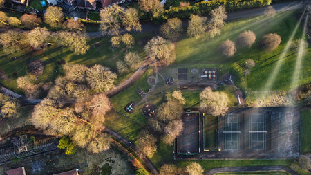 Scenic aerial view of a park featuring pathways, sports courts, and play areas surrounded by trees...