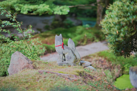 Stone fox statue adorned with a red scarf in a tranquil Japanese garden setting