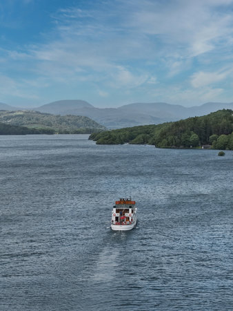Scenic boat ride across a tranquil lake surrounded by lush green hills and distant mountains on a clear dayの写真素材