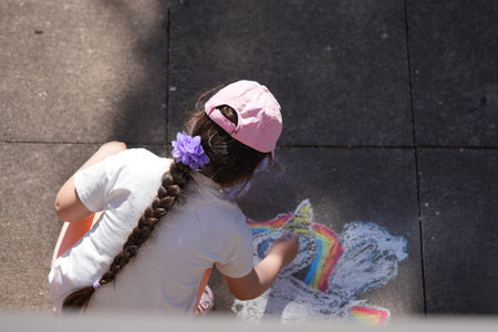 Little girl drawing colorful chalk art on pavement in a sunny outdoor settingの写真素材