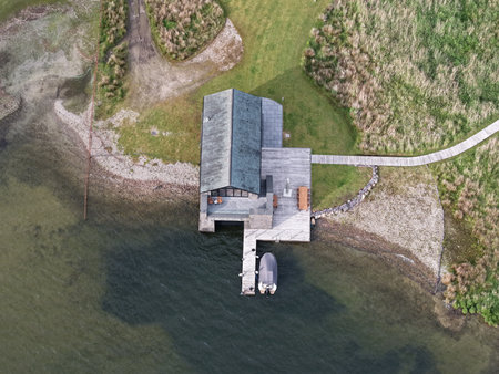 Cozy waterfront cabin with dock nestled in green landscape during bright daytimeの写真素材