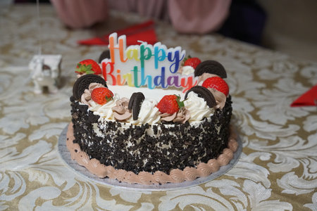 Celebrating a birthday with a colorful cake decorated with strawberries and cookies during an evening partyの写真素材