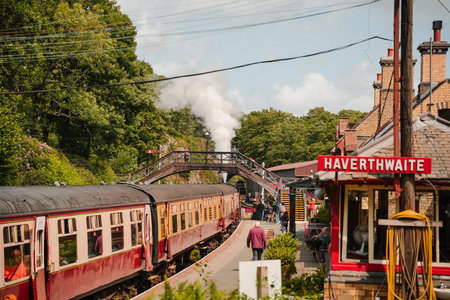 Steam train arrives at Havertwaiting station on a sunny day with trees in the background and...