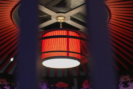 Bright red lantern illuminates traditional space adorned with ornate designs in a cultural venue at nightの写真素材