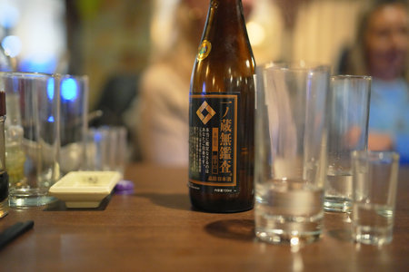 Sake bottle on a wooden table surrounded by empty glasses in a cozy restaurant setting at nightの写真素材