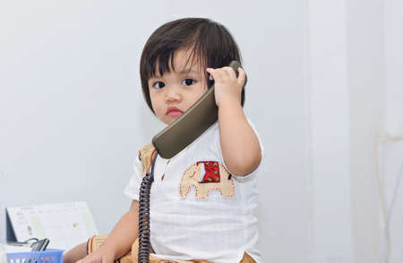 Asian  girl baby seating on work desk and play telephone.(Soft focus.)の写真素材