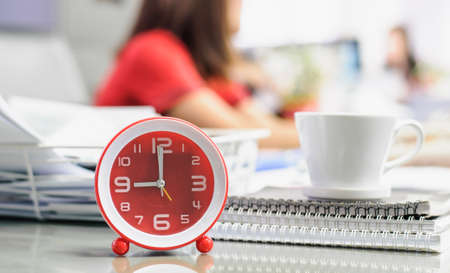 Alarm clock with coffee cup and notebook on desk in work office,soft focus.の写真素材