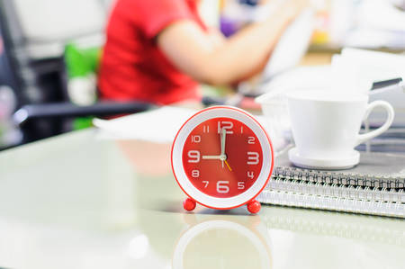 Alarm clock with coffee cup and notebook on desk in work office,soft focus.の写真素材