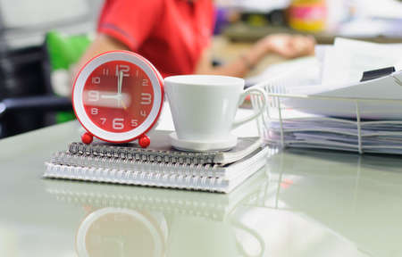 Alarm clock with coffee cup and notebook on desk in work office,soft focus.の写真素材