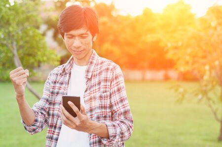 Happy asian man with news or message from smart phone in garden,soft focus,success concept.の写真素材
