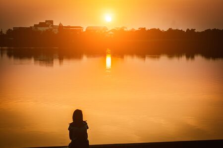 Woman sit near lake at sunset/ sunrise,selective focus,silhouette.の写真素材