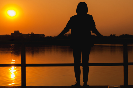 Young woman standing in park at sunset/ sunrise,silhouette.の写真素材