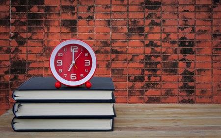 Old book and clock on wooden table and brick wall background,soft focus.