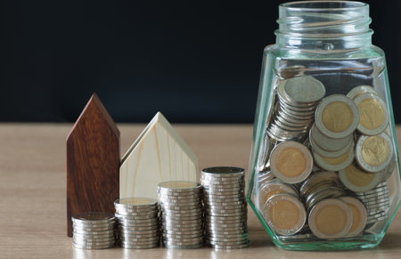 Saving concept,coin money in glass bottle with small wooden home on work desk,selective focus.の写真素材