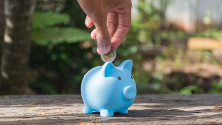 Hand holding coin and putting in piggy bank,save money concept,soft focus.の写真素材