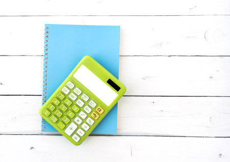 Green calaulator and blue notebook on white wood table.の写真素材