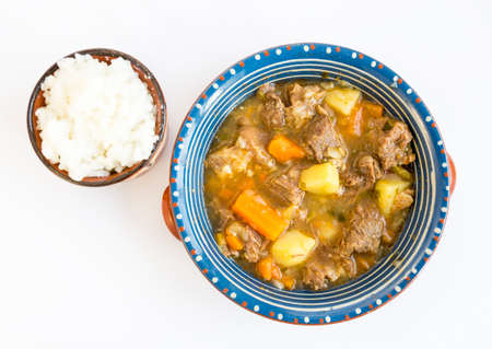 Beef stew with meat, potatoes and carrots in a ceramic dish with rice besides.の写真素材
