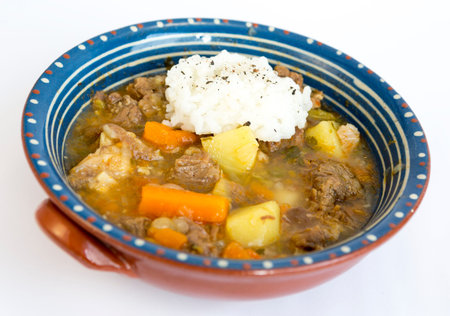 Beef stew with meat, potatoes and carrots in a ceramic dish with rice besides.の写真素材