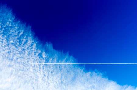 An airplane with its trail against the colorful blue sky with vloudsの写真素材