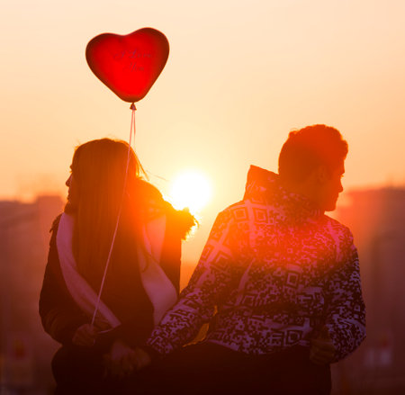 Sofia, Bulgaria - February 14, 2015: A silhouette of an young couple in love with a red heart shape balloon sitting on a bridge at the night of Valentine's Day.のeditorial素材