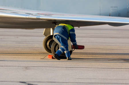 An airport worker is stabilizing the airplane tires on the airport runway after landing.の写真素材