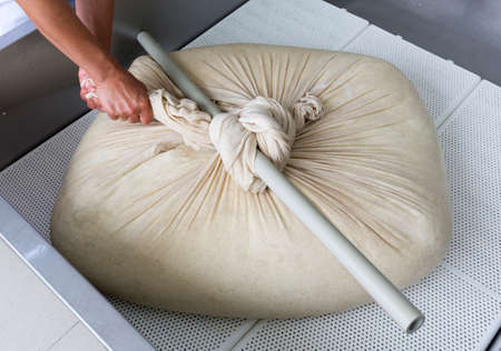 A woman working in a small family creamery is processing the final steps of making a cheese batch. The dairy farm is specialized in buffalo yoghurt and cheese production.の写真素材