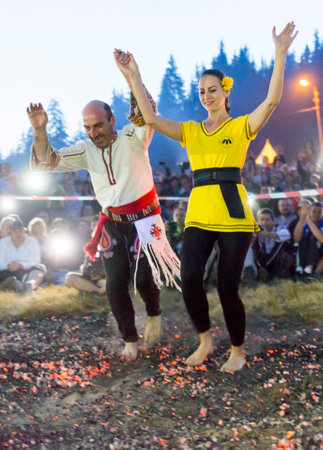 Rijen, Bulgaria - July 18, 2015: A nestinar woman with a child is walking on fire during a nestinarstvo show. The fire ritual involves a barefoot dance on smouldering embers performed by nestinari.のeditorial素材