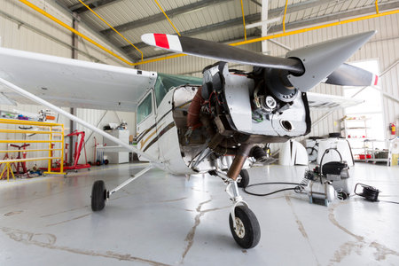 Small two-seated propeller airplane is being repaired in a hangar at the airport.
