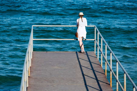 An young woman is watching the waters of Black sea from a pier in Sozopol, Bulgaria.の写真素材