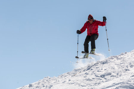 Sofia, Bulgaria - March 12, 2016: A free rider is jumping from the edge of a slope while skiing down a snowy rocky mountain top. Clear blue sky.のeditorial素材