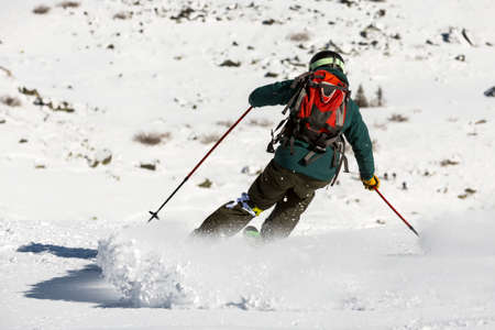 A free rider is skiing down a snowy rocky mountain top. A picture from his back. High speed.の写真素材
