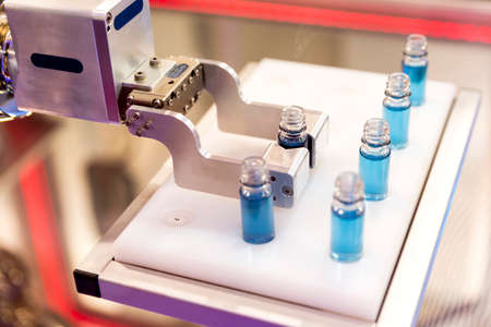 Robotic mechanical arm is manipulating chemical tubes full with blue substance in a medical laboratory during a test.の写真素材