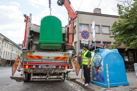 Sofia, Bulgaria - May 26, 2016: A sanitary worker is picking up trash bins with his recycling truck....