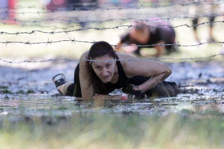 Sofia, Bulgaria - July 9, 2016: A participant is crawling through water under electrified wires at the Legion Run extreme sport challenge near Sofia. The sports event is mud and obstacle course designed to test people's physical strength, stamina, and menのeditorial素材