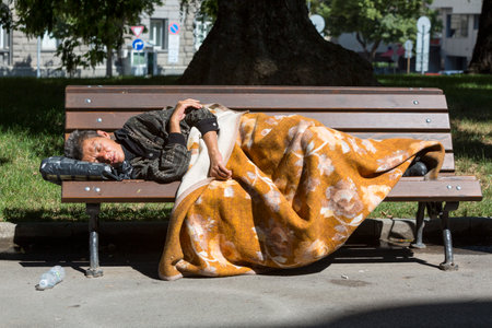 Sofia, Bulgaria - July 6, 2016: Homeless woman is sleeping on a bench in a park wrapped in blanket in the center of Sofia. Years after joining the EU Bulgaria is still the poorest country in the union.のeditorial素材