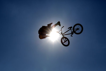 An extreme rider is making a free style jump from a ramp. The young boy with his bicycle is seen as...