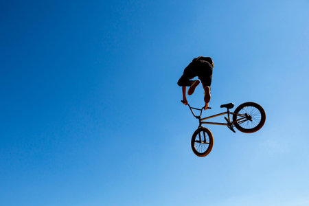 Silhouette of a biker jumping against the blue sky and the sun.