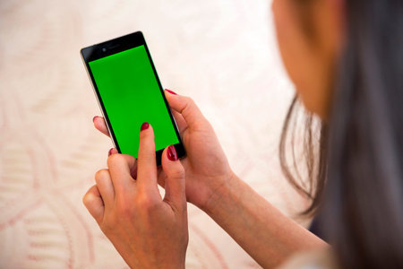 Young woman types and slides on her smartphone at home. Cellphone with chroma key screen - green...