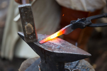 Blacksmith manually forging the molten metal. Blacksmith hammering hot metal arrow blade. Man in medieval clothes.の写真素材
