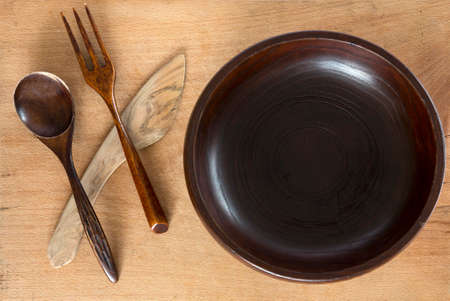 Wooden plate, spoon, fork and knife on a wooden background from above. Studio shot. Kitchen utensil.の写真素材