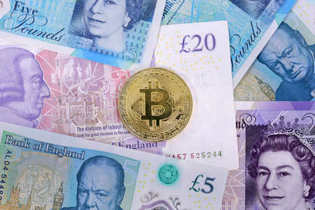Single virtual cryptocurrency money Bitcoin golden coin on United Kingdom Pound sterling banknotes with faces of Queen Elizabeth II and Winston Churchill.の写真素材