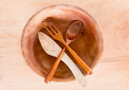 Wooden bowl with knife, spoon and fork on a wooden background from above. Studio shot. Kitchen utensil.の写真素材