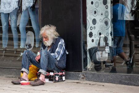 Sofia, Bulgaria - 7 May, 2018: Homeless old man with long white beard begs for money in front of clothes shop. Ten years after joining the EU Bulgaria is still the poorest country in the union.のeditorial素材