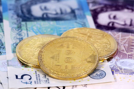 Three virtual cryptocurrency money Bitcoin golden coins on United Kingdom Pound sterling banknotes with faces of Queen Elizabeth II.の写真素材