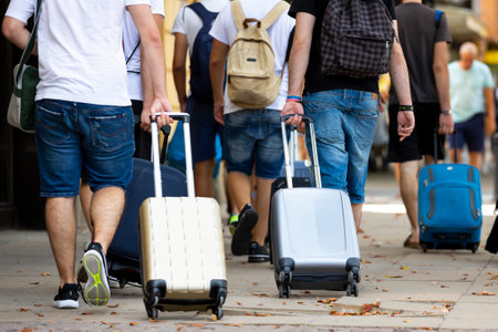 People with suitcases on wheels are seen from their backs on the street walking. Unrecognizable people.のeditorial素材