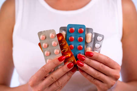 Different colorful pills and capsules in blisters in the hands of beautiful young woman. Global pharmaceutical industry for billions dollars per year. Pharmaceutical drugs for use as medications.の写真素材