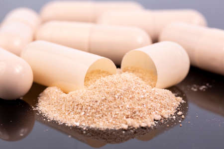 Some beige capsules and beige powder isolated on black reflective surface. Global pharmaceutical industry for billions dollars per year. Pharmaceutical drugs for use as medications. Studio macro shot.の写真素材