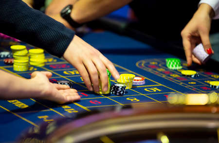 Roulette table with human hands putting down chips in casino. Roulette wheel in the foreground. Gamble game. Unrecognizable people.の写真素材