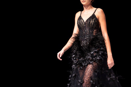 Female model walks the runway in black dress isolated on a black background during a Fashion Show. Fashion catwalk event showing new collection of clothes. Single female model in beautiful dress.のeditorial素材