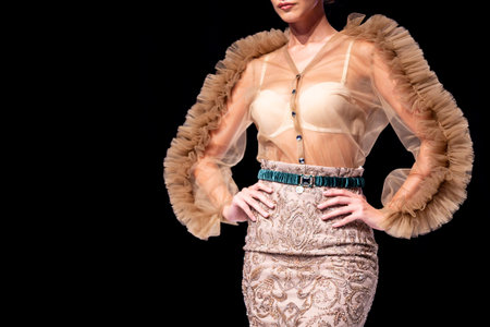 Female model walks the runway in beige skirt isolated on a black background during a Fashion Show....
